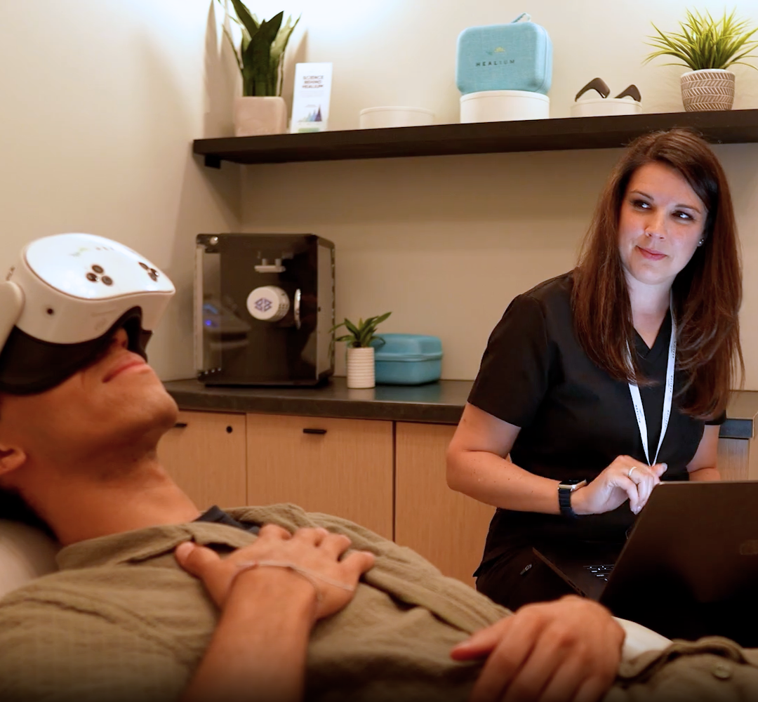 A person wearing a VR headset beside a clinician using a laptop
